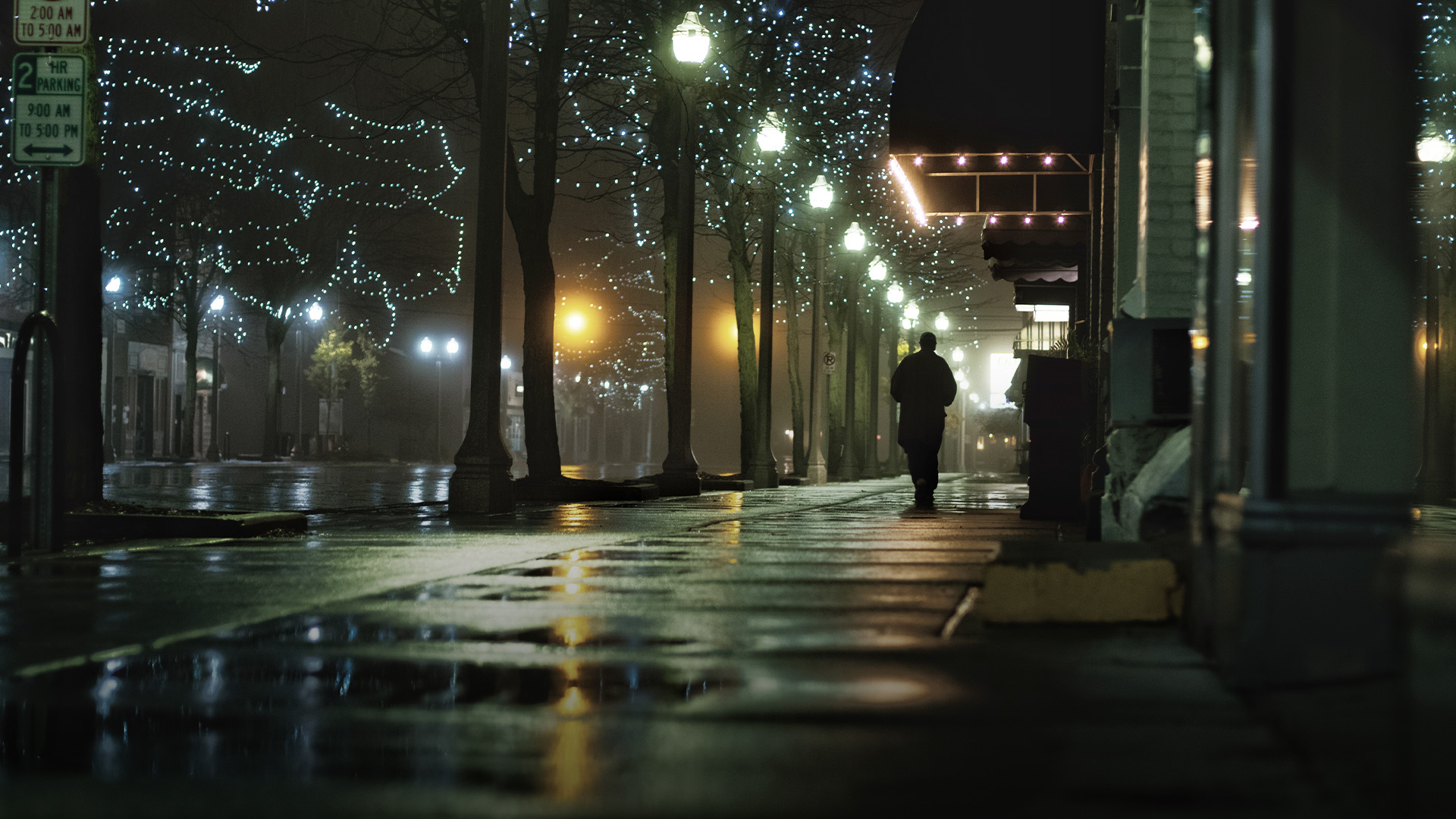 man walking alone on a lamp lit rainy night