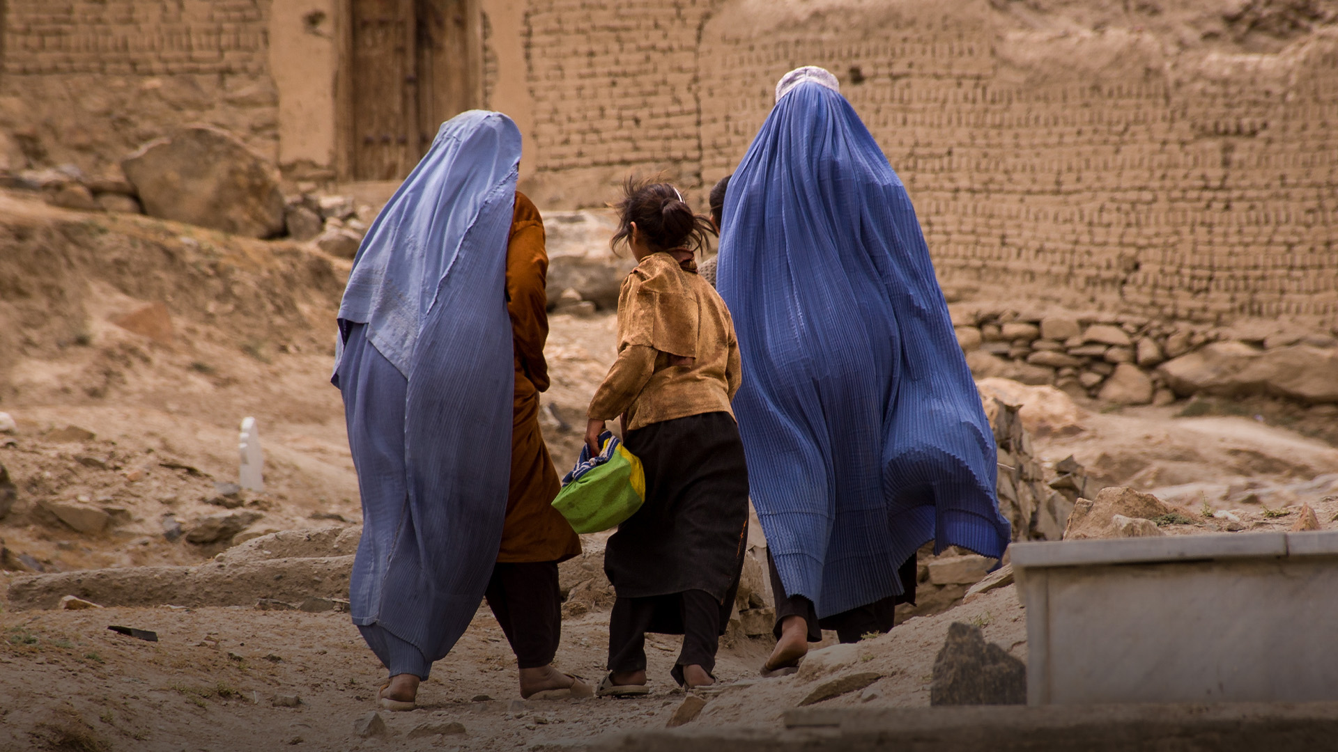 Girls and women in burqas walk through a graveyard near Kabul